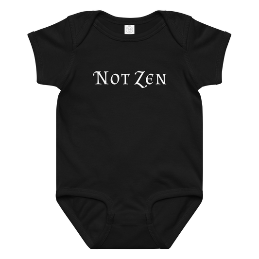 "Not zen" printed on a black baby jersey bodysuit laying on a flat surface amongst other clothes