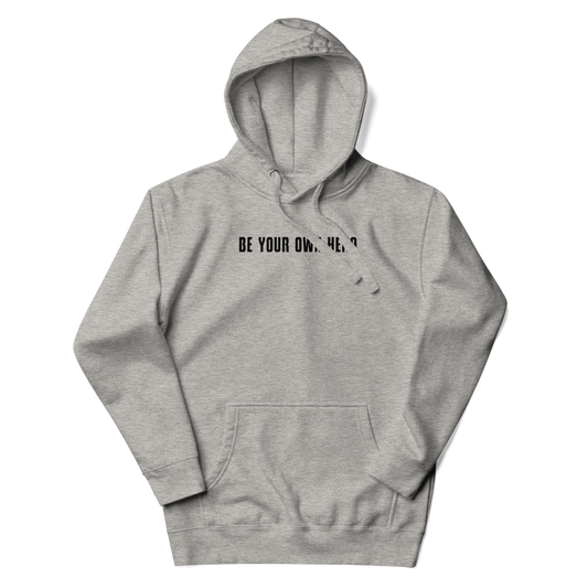"Be your own here" printed on a carbon grey unisex hoodie laying on a flat surface with the hood up