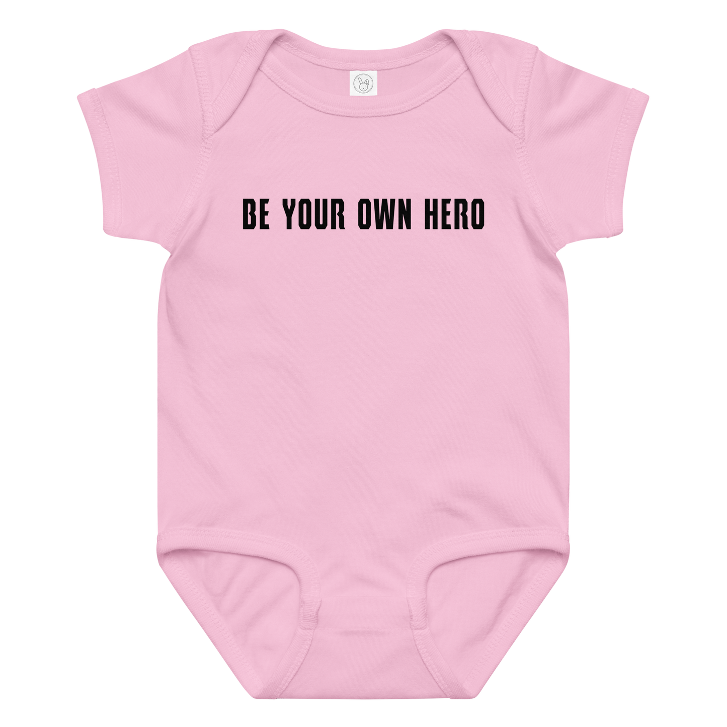 "Be your own here" printed on a pink baby jersey bodysuit laying on a flat surface amongst other clothes
