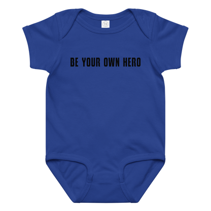 "Be your own here" printed on a royal baby jersey bodysuit laying on a flat surface amongst other clothes