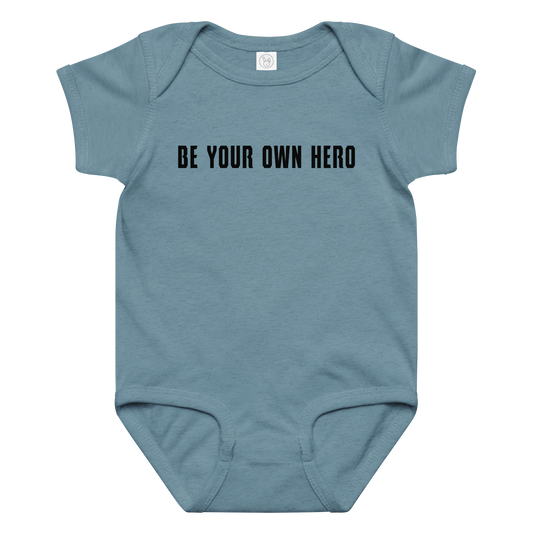 "Be your own here" printed on a vintage indigo baby jersey bodysuit laying on a flat surface amongst other clothes