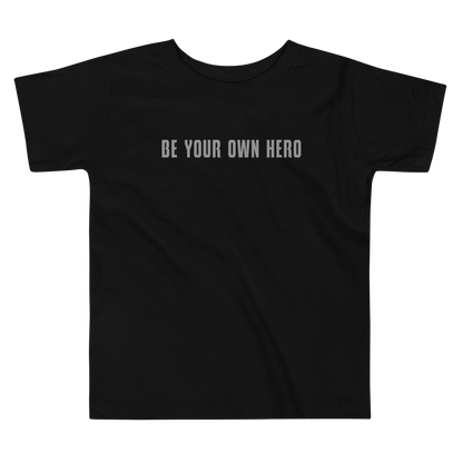 "Be your own here" printed on a black toddler short sleeve tee laying on a flat surface