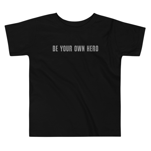 "Be your own here" printed on a black toddler short sleeve tee laying on a flat surface