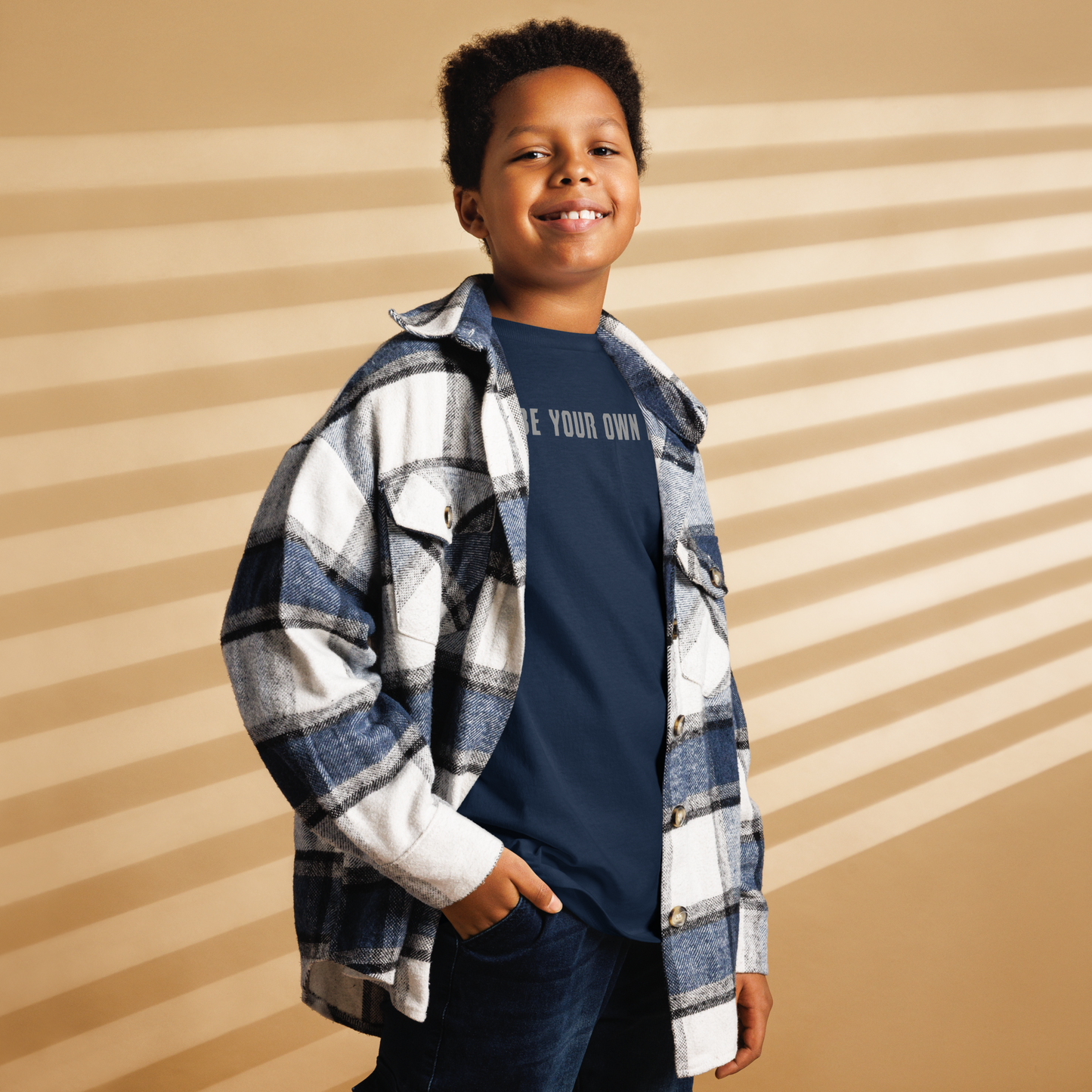 "Be your own here" printed on a navy youth classic tee worn by a male also wearing a jacket