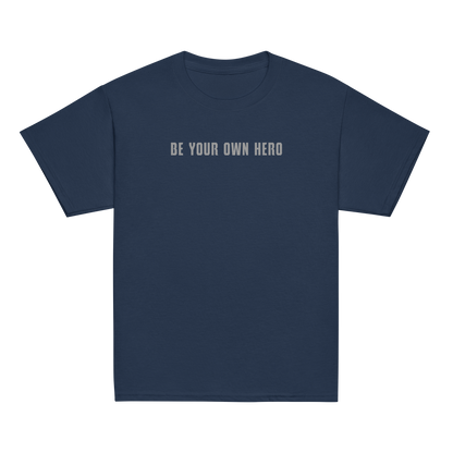 "Be your own here" printed on a navy youth classic tee laying on a flat surface