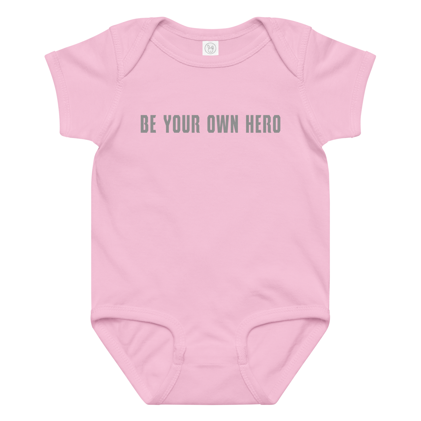 "Be your own here" printed on a pink baby jersey bodysuit laying on a flat surface amongst other clothes