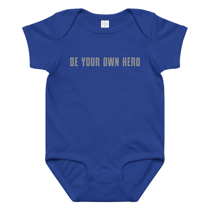 "Be your own here" printed on a royal baby jersey bodysuit laying on a flat surface amongst other clothes