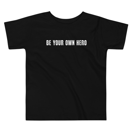 "Be your own here" printed on a black toddler short sleeve tee laying on a flat surface