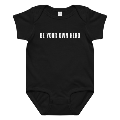 "Be your own here" printed on a black baby jersey bodysuit laying on a flat surface amongst other clothes