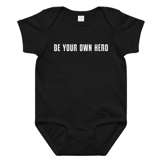 "Be your own here" printed on a black baby jersey bodysuit laying on a flat surface amongst other clothes
