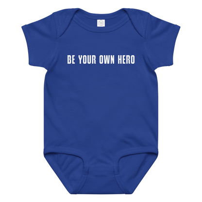 "Be your own here" printed on a royal baby jersey bodysuit laying on a flat surface amongst other clothes
