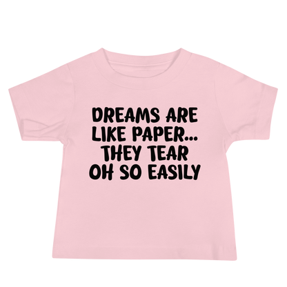 "Dreams are like paper, they tear oh so easily" printed on a pink baby jersey short sleeve tee laying on a flat surface