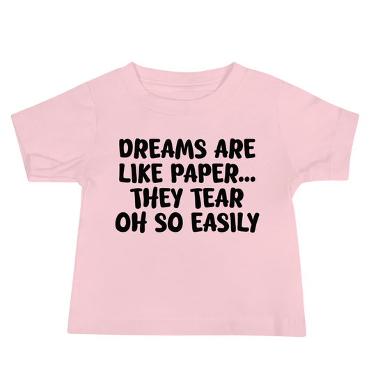 "Dreams are like paper, they tear oh so easily" printed on a pink baby jersey short sleeve tee laying on a flat surface