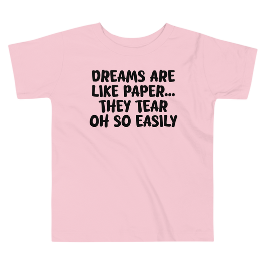"Dreams are like paper, they tear oh so easily" printed on a pink toddler short sleeve tee laying on a flat surface