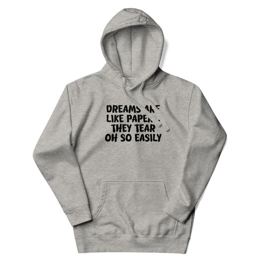 "Dreams are like paper, they tear oh so easily" printed on a carbon grey unisex hoodie laying on a flat surface with the hood up