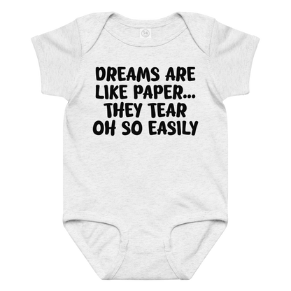 "Dreams are like paper, they tear oh so easily" printed on a ash baby jersey bodysuit laying on a flat surface amongst other clothes