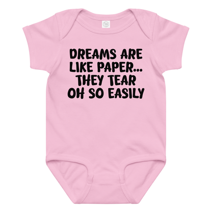 "Dreams are like paper, they tear oh so easily" printed on a pink baby jersey bodysuit laying on a flat surface amongst other clothes