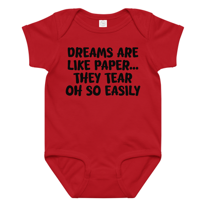 "Dreams are like paper, they tear oh so easily" printed on a red baby jersey bodysuit laying on a flat surface amongst other clothes