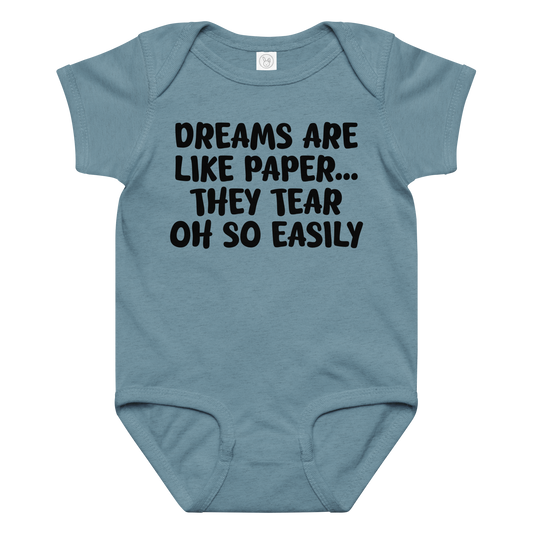 "Dreams are like paper, they tear oh so easily" printed on a vintage indigo baby jersey bodysuit laying on a flat surface amongst other clothes