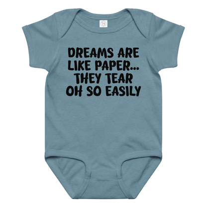 "Dreams are like paper, they tear oh so easily" printed on a vintage indigo baby jersey bodysuit laying on a flat surface amongst other clothes