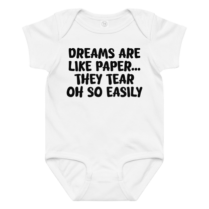 "Dreams are like paper, they tear oh so easily" printed on a white baby jersey bodysuit laying on a flat surface amongst other clothes