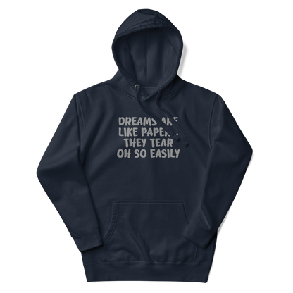 "Dreams are like paper, they tear oh so easily" printed on a navy blazer unisex hoodie laying on a flat surface with the hood up