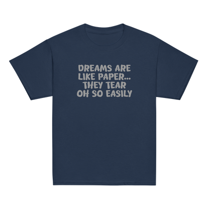 "Dreams are like paper, they tear oh so easily" printed on a navy youth classic tee laying on a flat surface