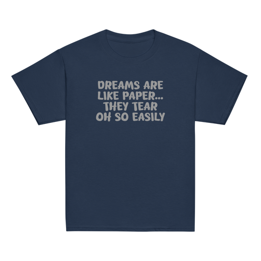 "Dreams are like paper, they tear oh so easily" printed on a navy youth classic tee laying on a flat surface