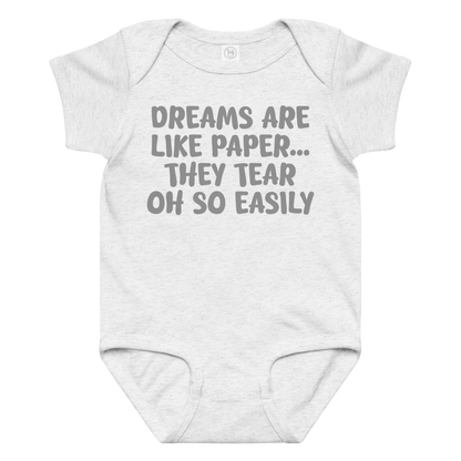 "Dreams are like paper, they tear oh so easily" printed on a ash baby jersey bodysuit laying on a flat surface amongst other clothes