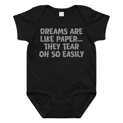 "Dreams are like paper, they tear oh so easily" printed on a black baby jersey bodysuit laying on a flat surface amongst other clothes