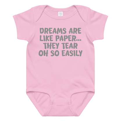 "Dreams are like paper, they tear oh so easily" printed on a pink baby jersey bodysuit laying on a flat surface amongst other clothes