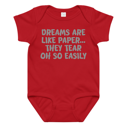 "Dreams are like paper, they tear oh so easily" printed on a red baby jersey bodysuit laying on a flat surface amongst other clothes