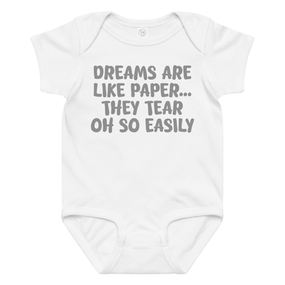 "Dreams are like paper, they tear oh so easily" printed on a white baby jersey bodysuit laying on a flat surface amongst other clothes