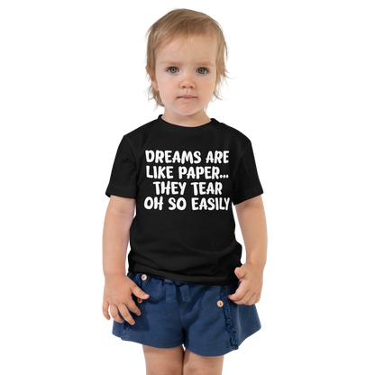 "Dreams are like paper, they tear oh so easily" printed on a black toddler short sleeve tee worn by a female