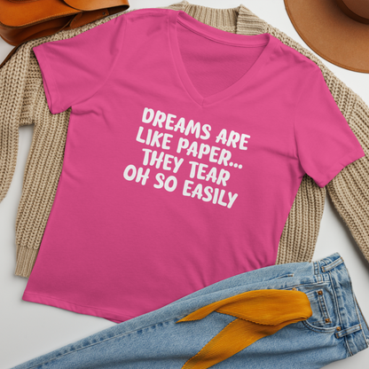 "Dreams are like paper, they tear oh so easily" printed on a berry women's relaxed v-neck t-shirt laying on a flat surface amongst other clothes