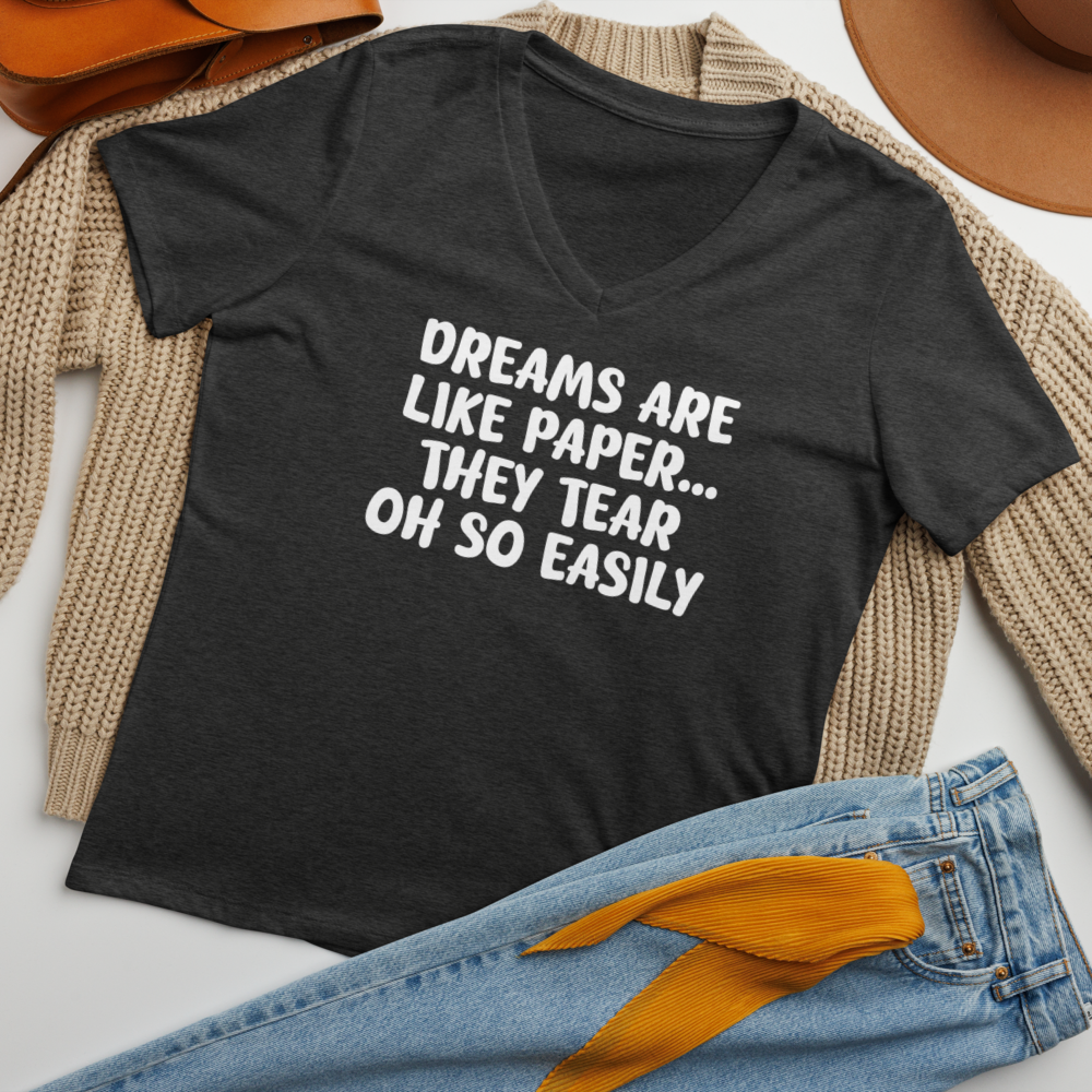 "Dreams are like paper, they tear oh so easily" printed on a dark grey heather women's relaxed v-neck t-shirt laying on a flat surface amongst other clothes