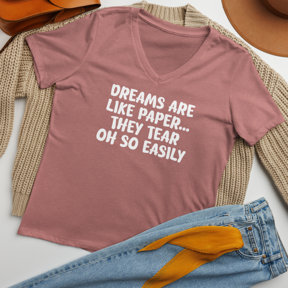 "Dreams are like paper, they tear oh so easily" printed on a heather mauve women's relaxed v-neck t-shirt laying on a flat surface amongst other clothes