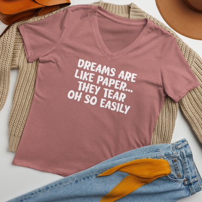 "Dreams are like paper, they tear oh so easily" printed on a heather mauve women's relaxed v-neck t-shirt laying on a flat surface amongst other clothes