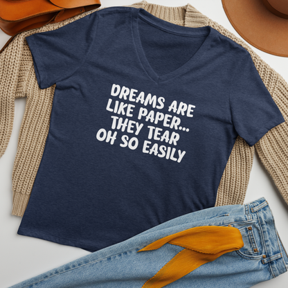 "Dreams are like paper, they tear oh so easily" printed on a heather navy women's relaxed v-neck t-shirt laying on a flat surface amongst other clothes