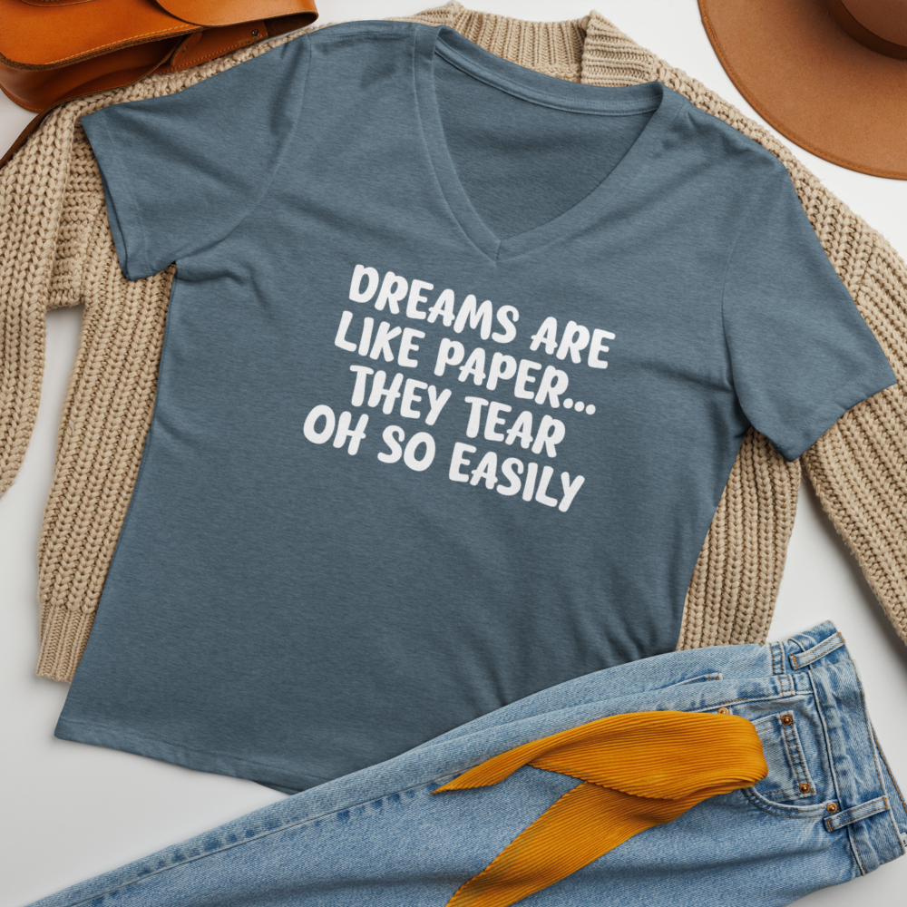"Dreams are like paper, they tear oh so easily" printed on a heather slate women's relaxed v-neck t-shirt laying on a flat surface amongst other clothes