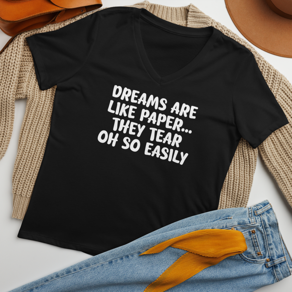 "Dreams are like paper, they tear oh so easily" printed on a solid black blend women's relaxed v-neck t-shirt laying on a flat surface amongst other clothes