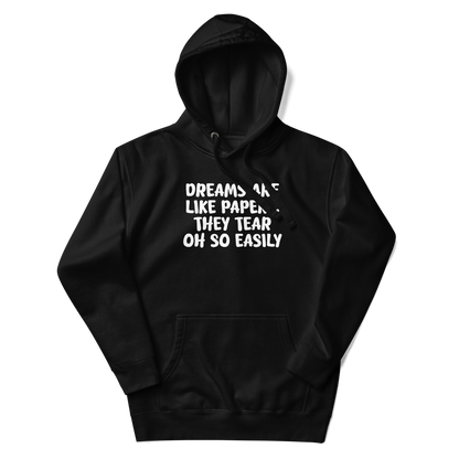 "Dreams are like paper, they tear oh so easily" printed on a black unisex hoodie laying on a flat surface with the hood up