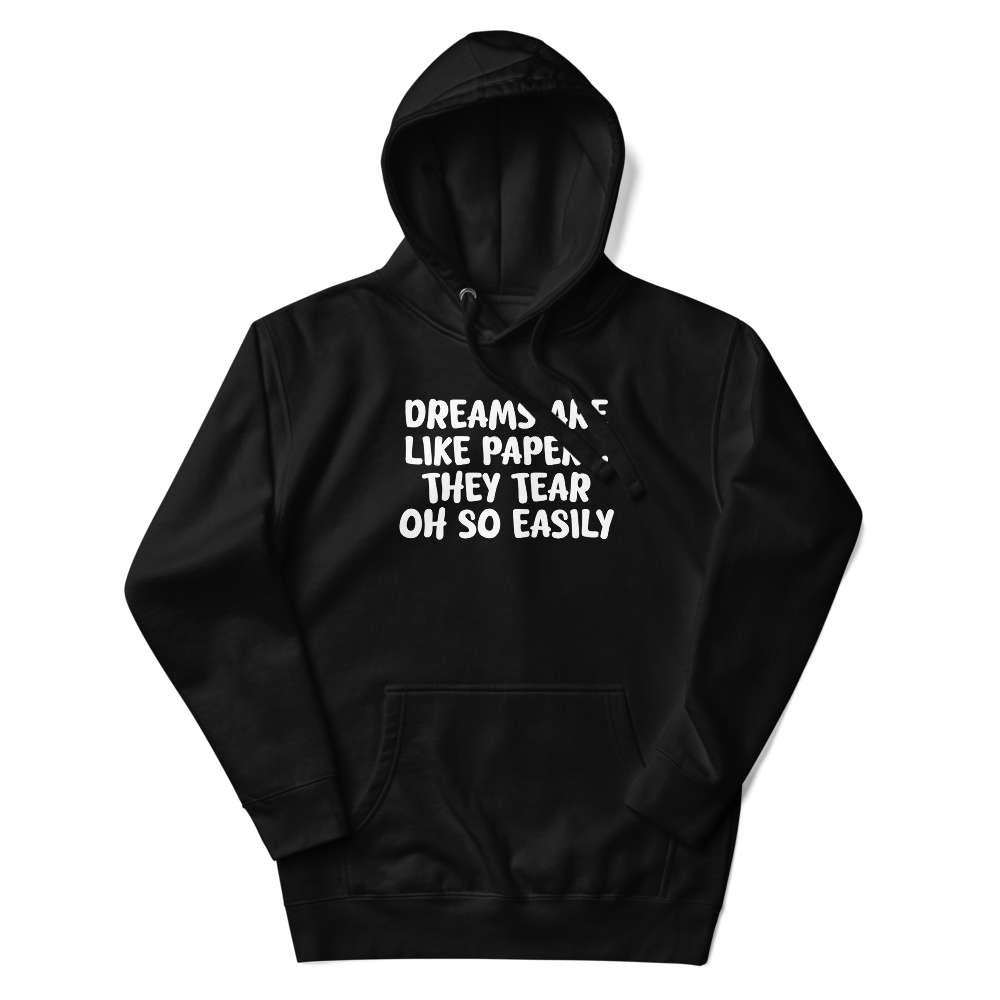 "Dreams are like paper, they tear oh so easily" printed on a black unisex hoodie laying on a flat surface with the hood up