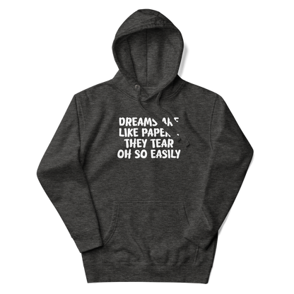 "Dreams are like paper, they tear oh so easily" printed on a charcoal heather unisex hoodie laying on a flat surface with the hood up