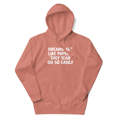 "Dreams are like paper, they tear oh so easily" printed on a dusty rose unisex hoodie laying on a flat surface with the hood up