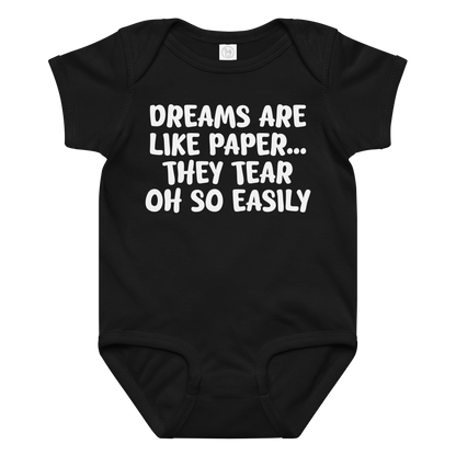 "Dreams are like paper, they tear oh so easily" printed on a black baby jersey bodysuit laying on a flat surface amongst other clothes
