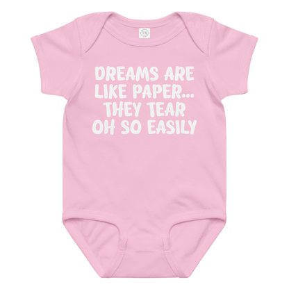 "Dreams are like paper, they tear oh so easily" printed on a pink baby jersey bodysuit laying on a flat surface amongst other clothes