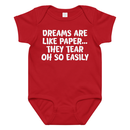 "Dreams are like paper, they tear oh so easily" printed on a red baby jersey bodysuit laying on a flat surface amongst other clothes