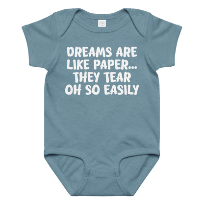 "Dreams are like paper, they tear oh so easily" printed on a vintage indigo baby jersey bodysuit laying on a flat surface amongst other clothes