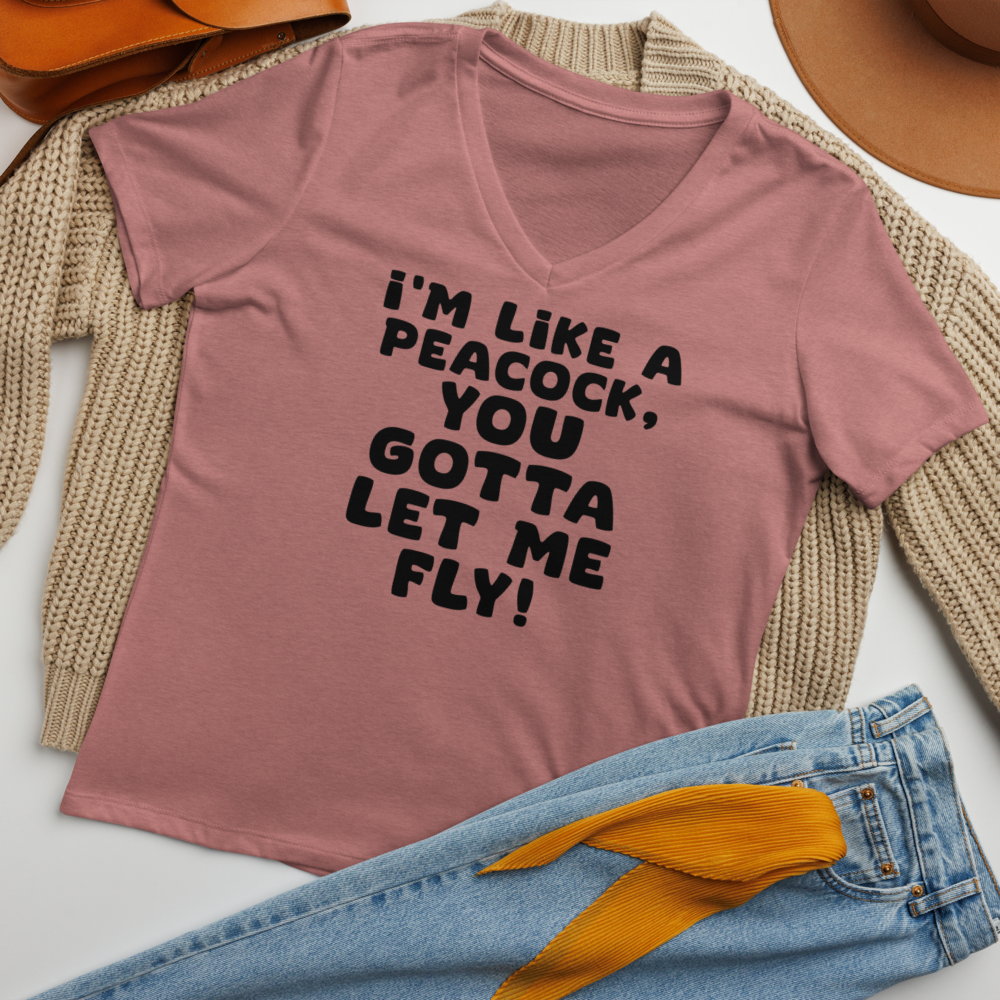 "I'm like a peacock, you gotta let me fly!" printed on a heather mauve women's relaxed v-neck t-shirt laying on a flat surface amongst other clothes